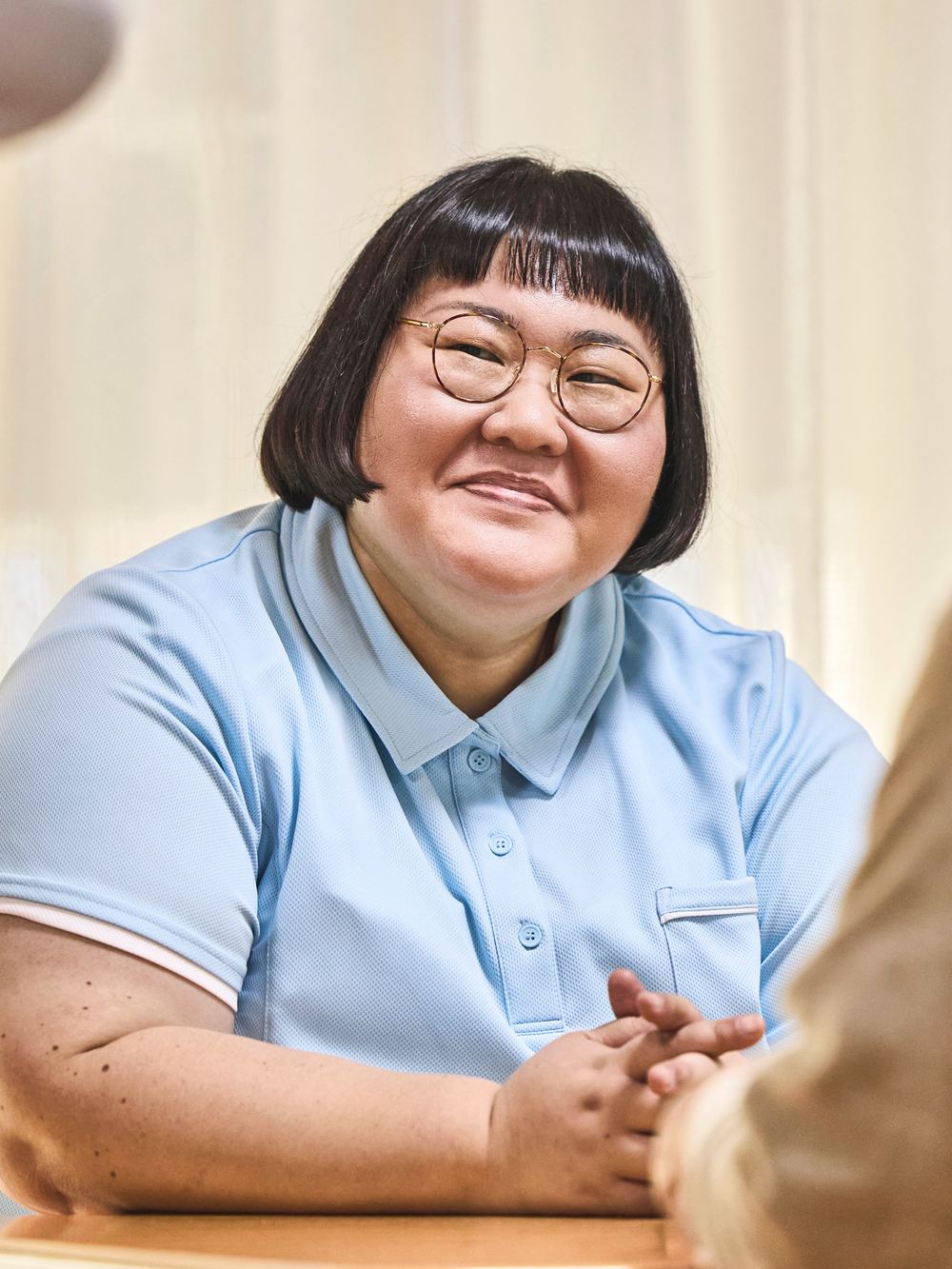 戸田伊月を演じる安藤なつ。入居者と向かい合い、やわらかく微笑む。
