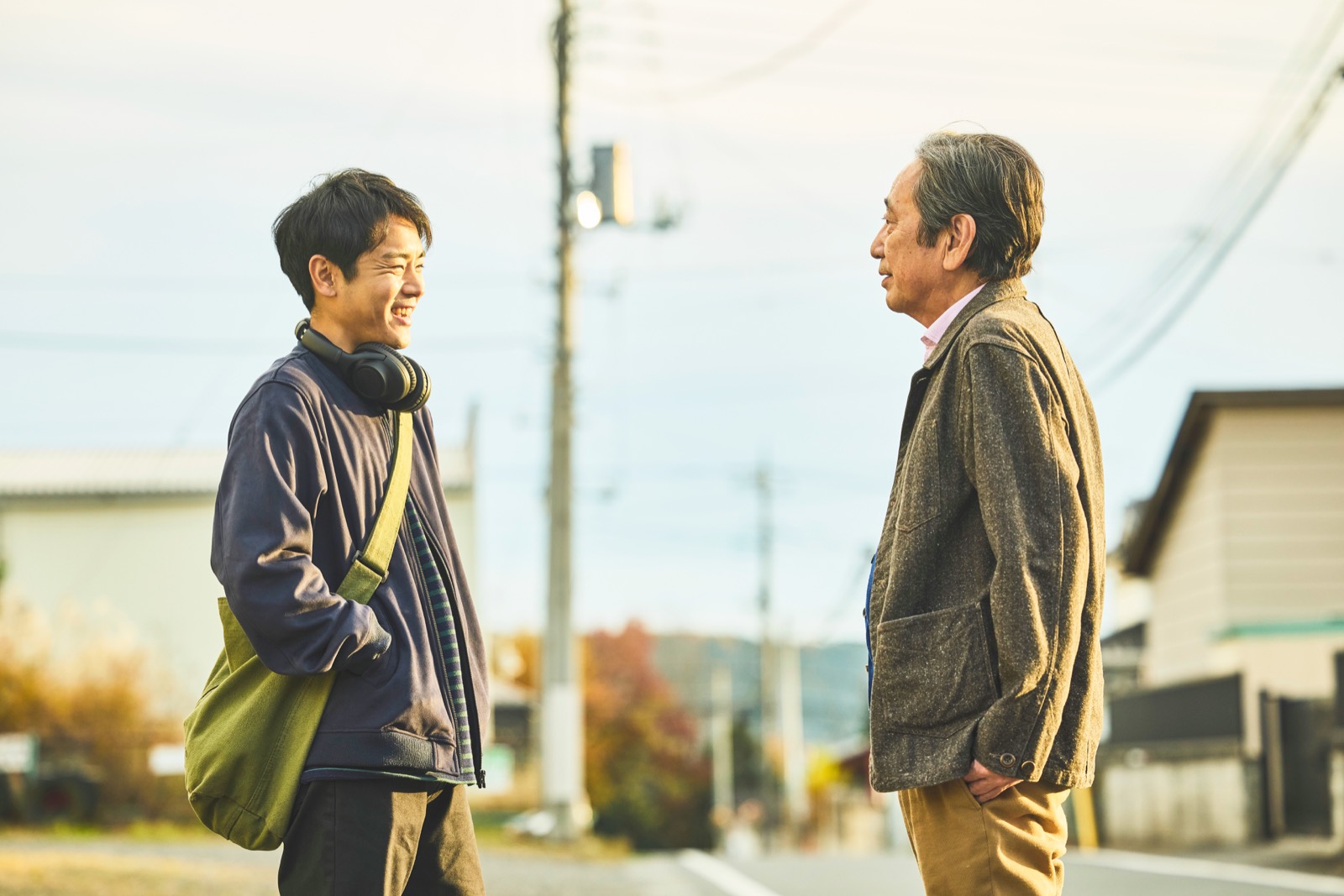 秋の住宅街の道で、向かい合って笑う優輝と豊。