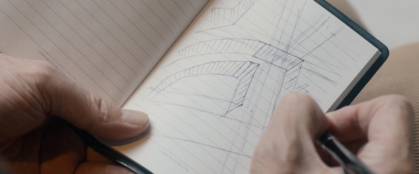 手帳に鉛筆で建物のスケッチを描く手元。